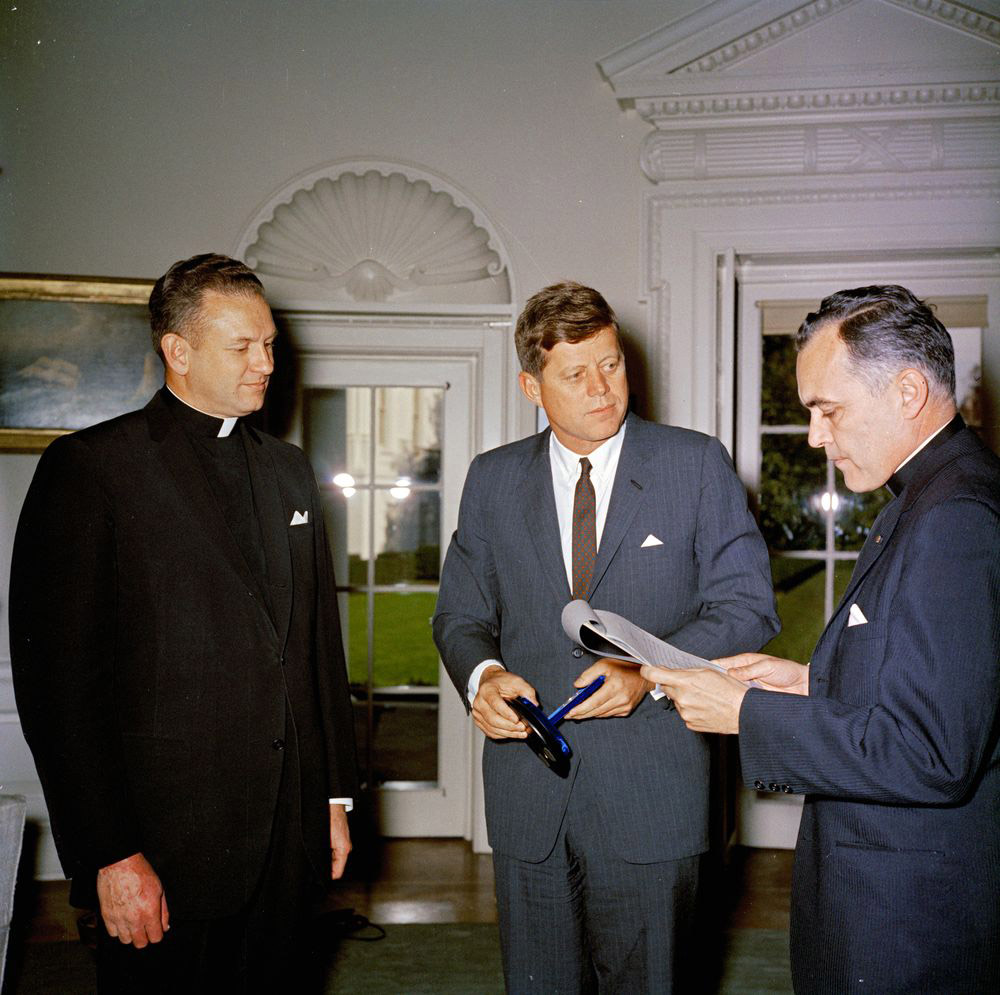 everend Theodore M. Hesburgh (right), president of the University of Notre Dame, delivers remarks at the presentation of the Laetare Medal for 1961 from the University of Notre Dame to President John F. Kennedy. Father Edmund P. Joyce, vice president of the University of Notre Dame, looks on. Oval Office, White House, Washington, D.C. 22 November 1961. (Photo: Photo: Robert Knudsen. JFK  Presidential Library and Museum.)