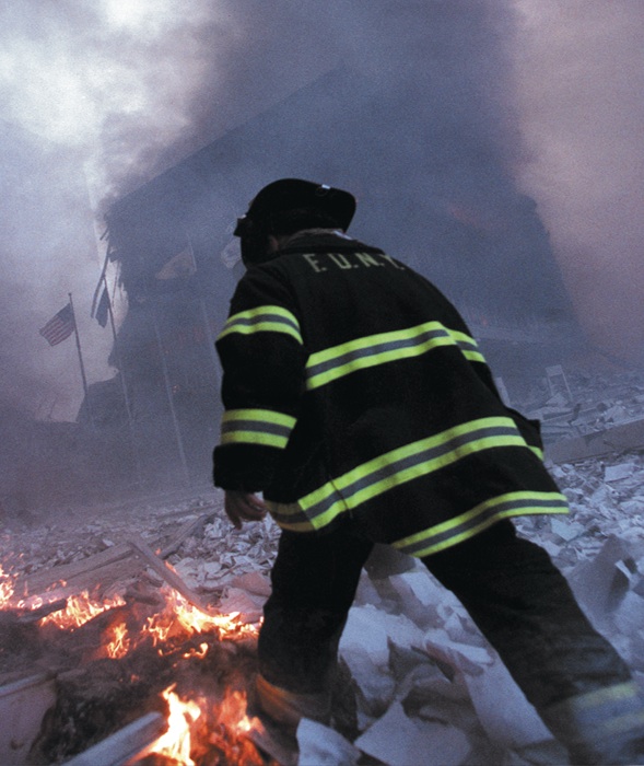 A firefighter walks through the burning rubble as toxic fumes fill the air.