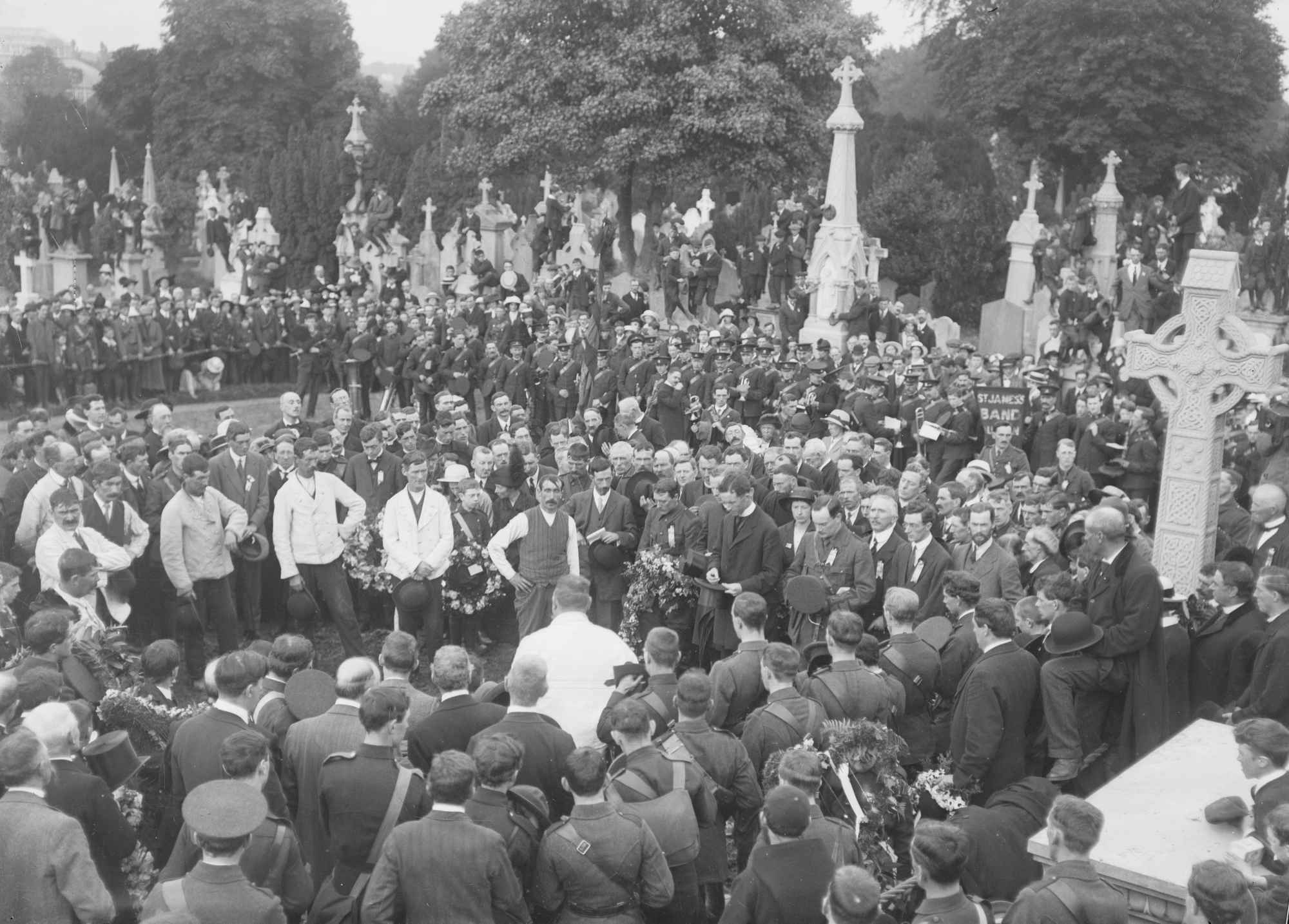 O’Donovan Rossa’s funeral at  Glasnevin Cemetery in Dublin, with Pádraig Pearse (standing to the right of the priest, his hat in front of him), John MacBride (to the right of Pearse), and Tom Clarke (three to the right of MacBride, in profile).