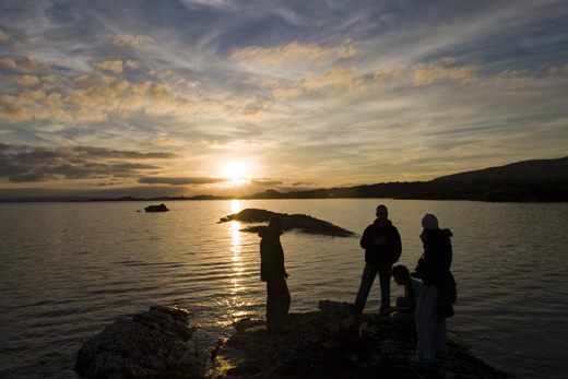 Friends lighting an evening bonfire on the shore of Kenmare Bay, County Kerry.