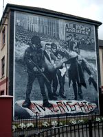 Bogside mural on Lecky Street, Londonderry. The mural depicts the famous photo of Father Edward Daly, waving a blood-stained white handkerchief as he escorts a mortally-wounded protester to safety during the events of Bloody Sunday (1972) in Derry, Northern Ireland. Photo: Wikipedia