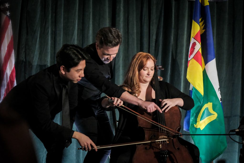 Violinist Gregory Harrington (center) with cellists Ian Lum, and Sara Scanlon (seated) performing Ravel’s “Boléro” on one cello. 